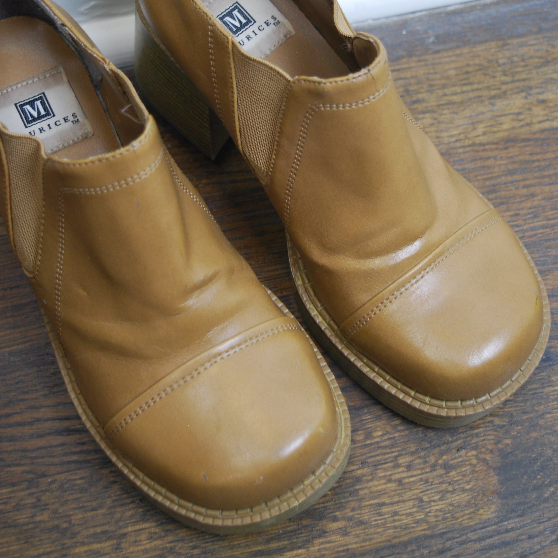Pair of tan shoes on a wooden floor with a white baseboard.