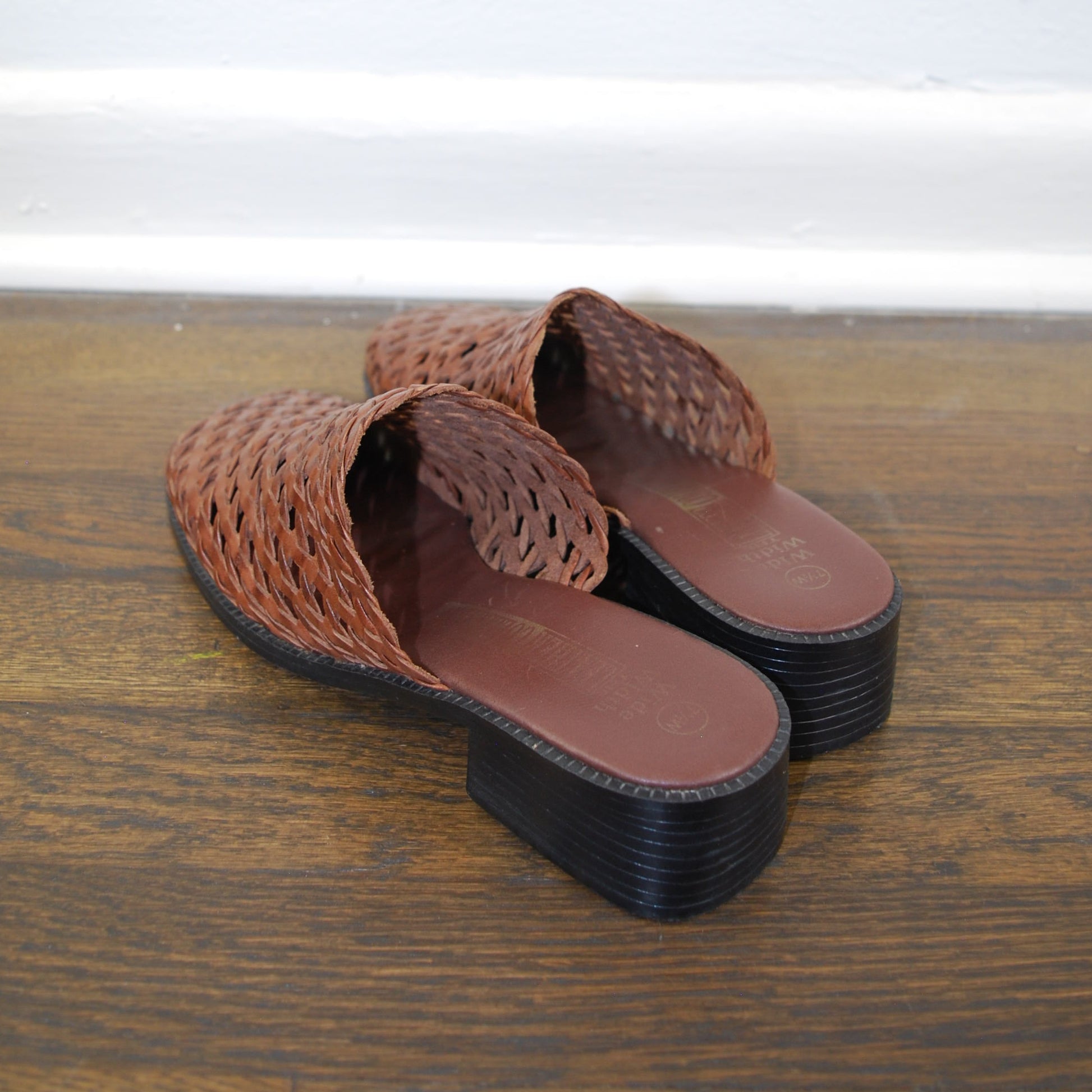 Brown woven sandal with black sole on a wooden floor