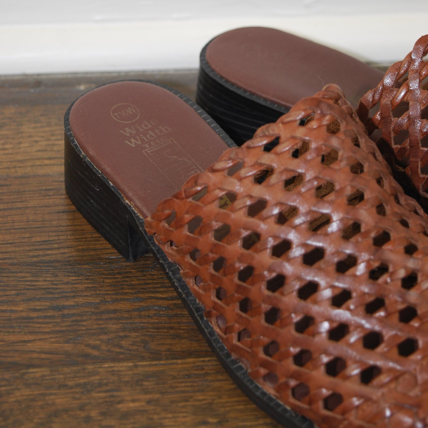 Brown perforated shoe with a brand logo on a wooden surface
