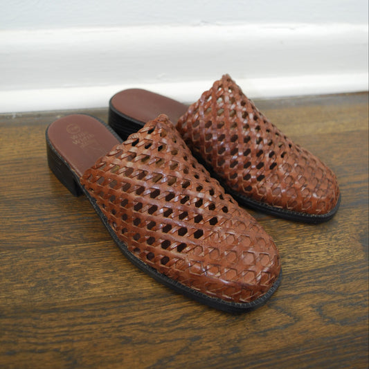 Brown perforated loafers on a wooden floor with a white wall background