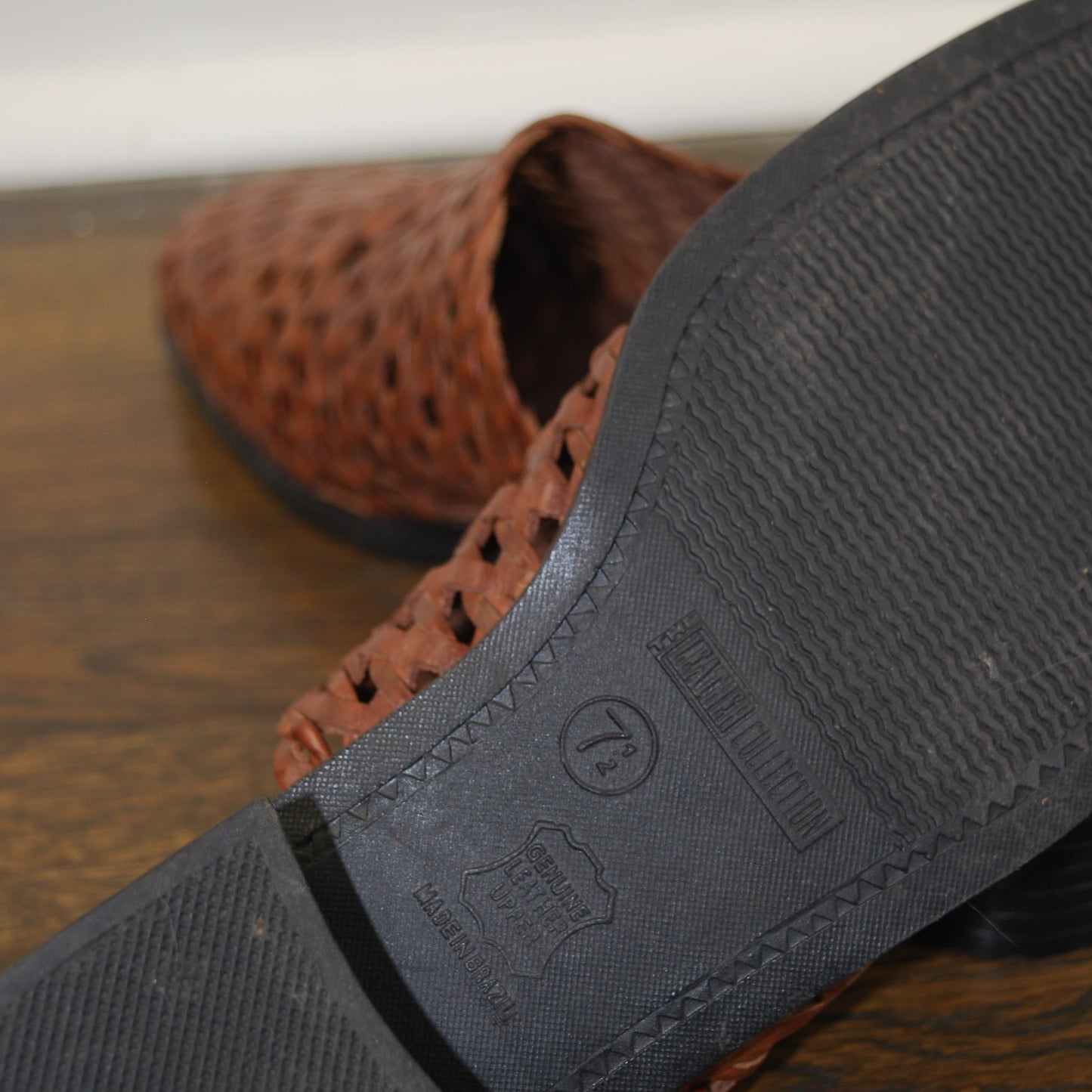 Close-up of a brown sandal with a black sole on a wooden surface.