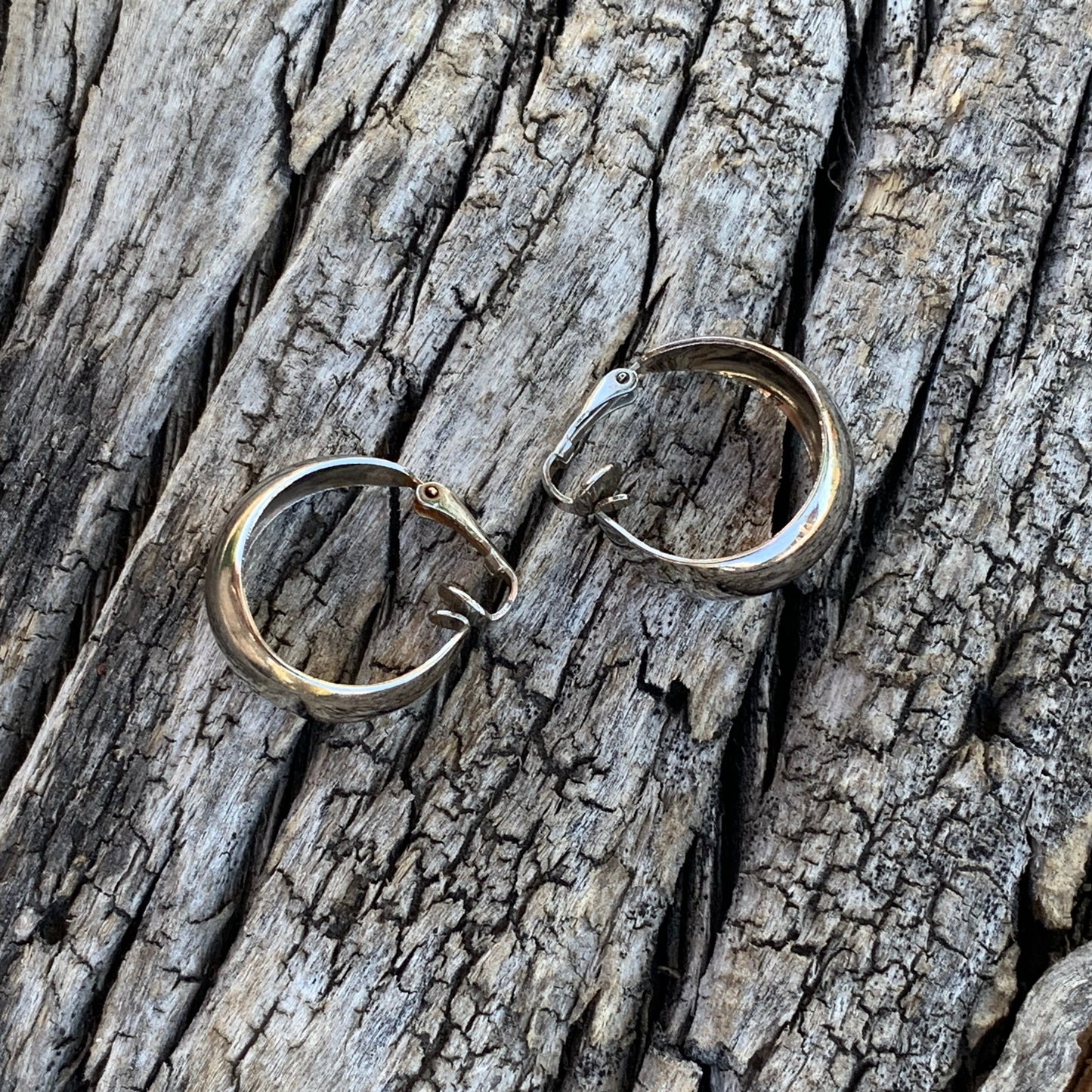 Pair of silver earrings on a textured wooden surface