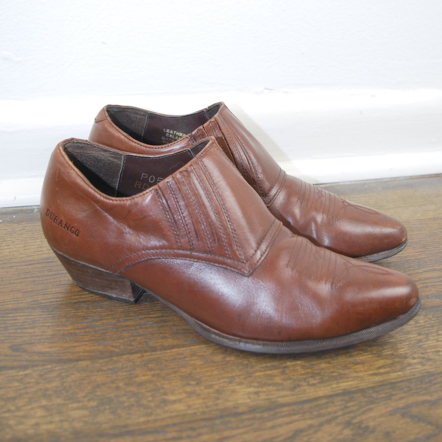 Pair of brown leather shoes on a wooden floor with a white wall background