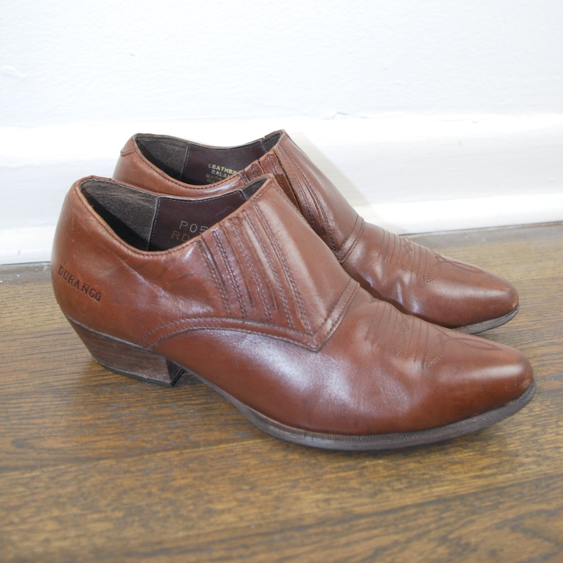Pair of brown leather shoes on a wooden floor with a white wall background