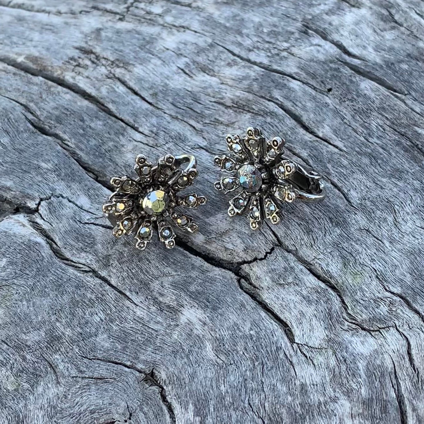Pair of silver floral earrings on a textured stone surface