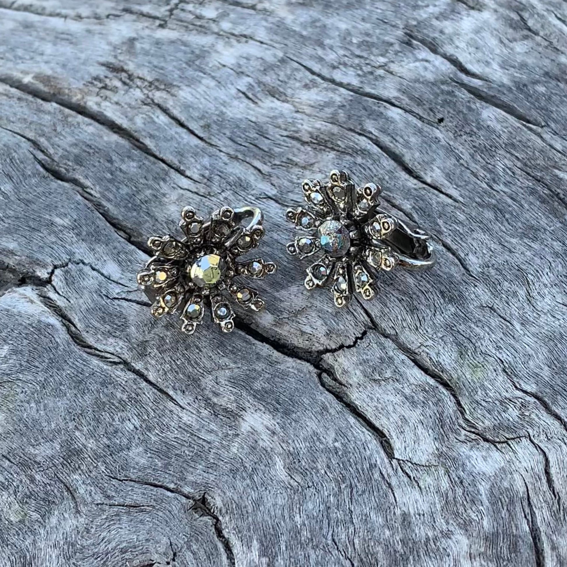 Pair of silver floral earrings on a textured stone surface