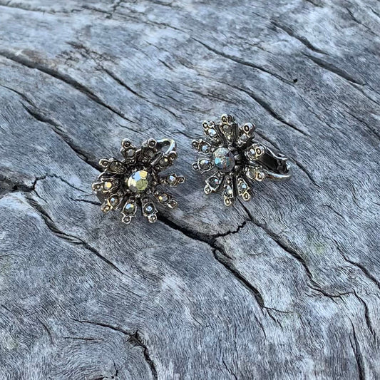 Pair of silver floral earrings on a textured stone surface