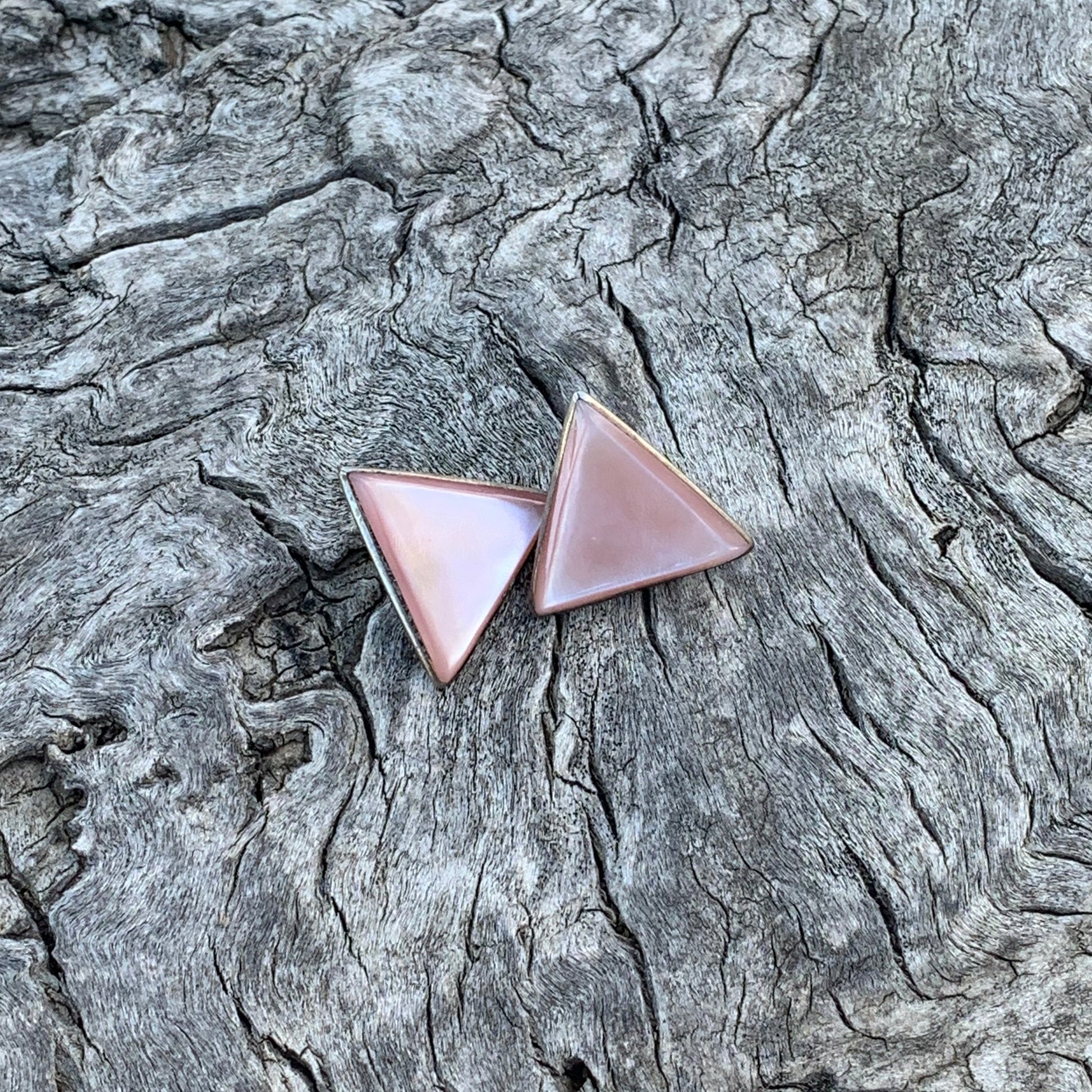 Two triangular earrings on a textured tree bark background