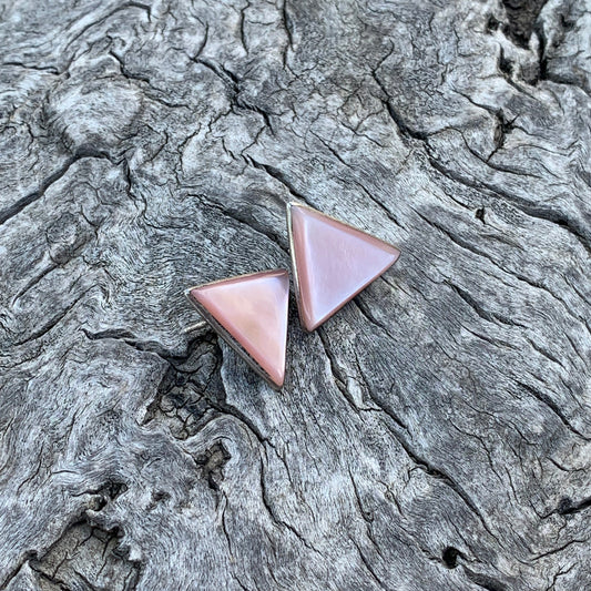Two pink triangle-shaped earrings on a textured stone surface